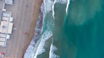 Spiaggia attrezzata vista dall'alto nel Lazio, con ombrelloni ordinati e onde che si infrangono sulla riva